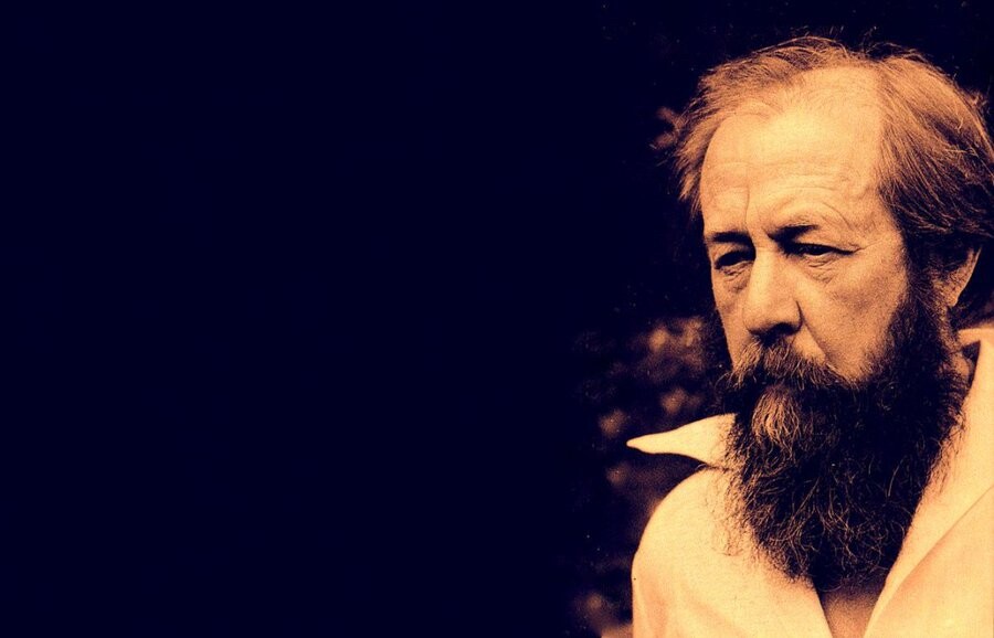 Sepia-toned photo of Aleksandr Solzhenitsyn in middle age, hairline receeded, bearded, in an open-collar shirt, a tired expression on his face.